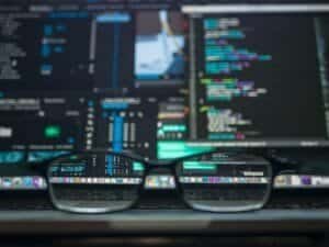Close-up of coding and software development on multiple screens with glasses on keyboard.