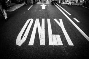 Black and white image of a painted stop sign on asphalt road, with pedestrians walking nearby.