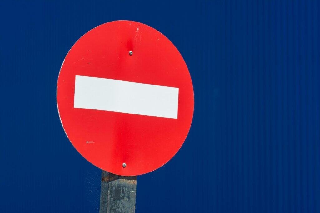 Close-up of a red no entry traffic sign against a vivid blue background.