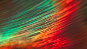 Blog Bright, vibrant digital art featuring holographic fiber optic strands in green, red, orange, and yellow.