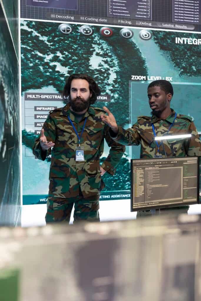 Alt text: Two military personnel in camouflage discussing digital display at a tech conference.