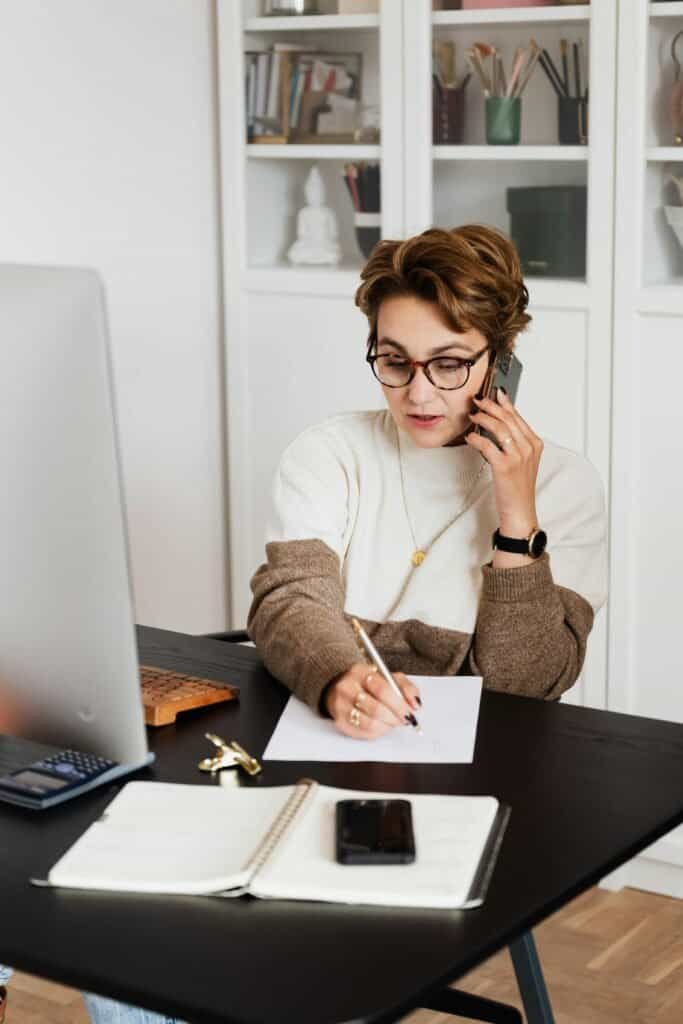 Business woman on phone with documents and laptop at desk in office.